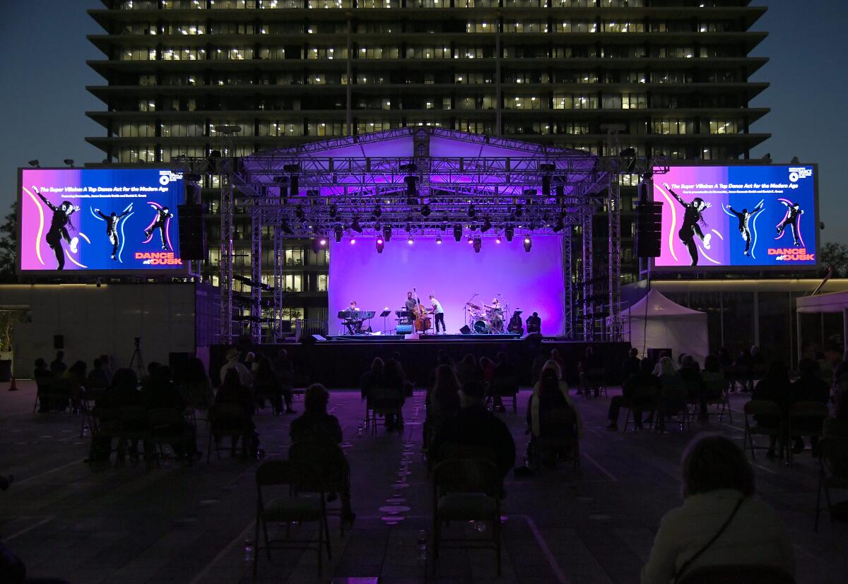 The Super Villainz dance on a lighted stage with the DWP Building as a backdrop.