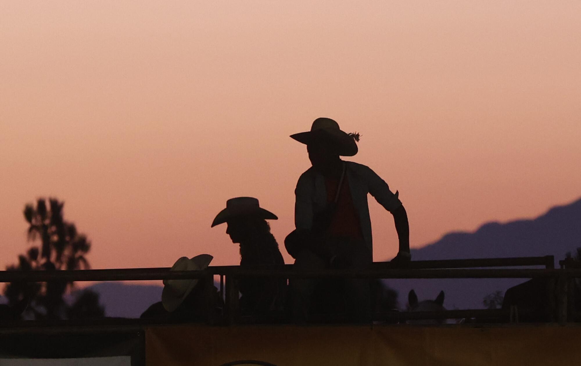 People in cowboy hats are silhouetted against a dusty sky.