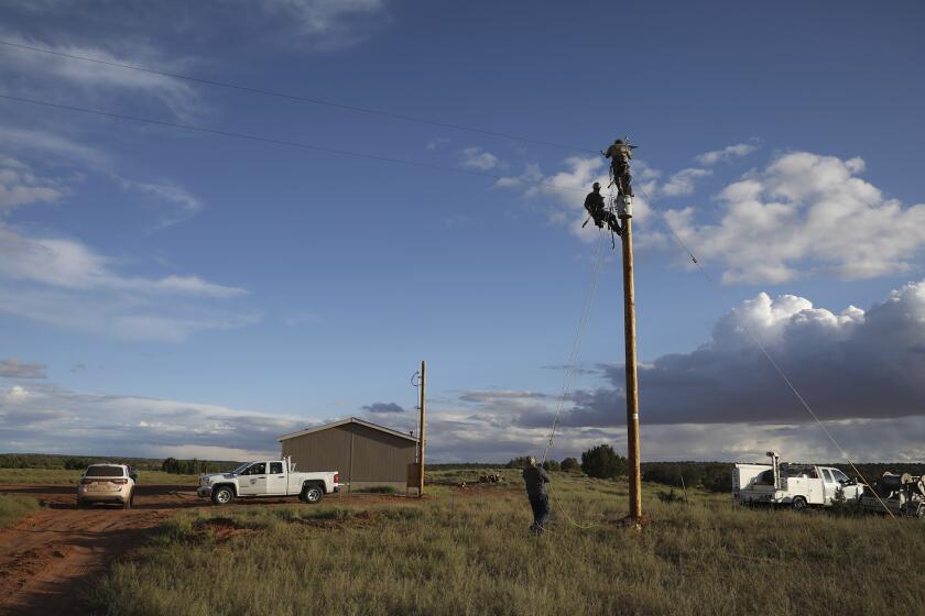 In this Wednesday, May 8, 2019 photo, utility workers prepare a power pole to connect a home in Kaibeto on the Navajo Nation to the electric grid. Miranda Haskie and her husband Jimmie Long Jr. have lived in the home with their son Jayden Long, 13, for more than a decade without electricity. An ambitious project to connect homes to the electric grid on the country's largest American Indian reservation is wrapping up. Utility crews from across the U.S. have volunteered their time over the past few weeks to hook up about 300 homes on the Navajo Nation. (AP Photo/Jake Bacon)