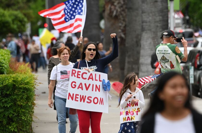 A woman raises her fist while shouting with a sign that says Recall Gavin Newsom