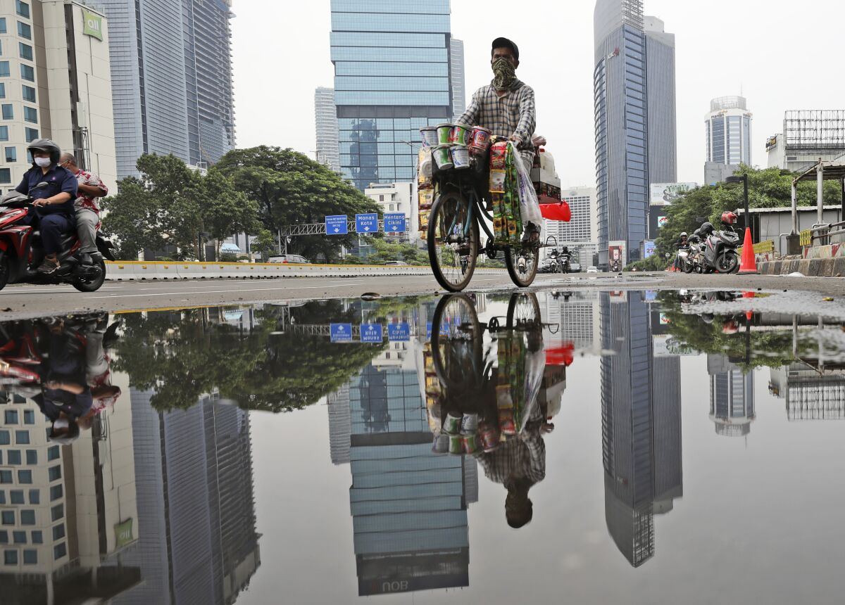 A drink vendor rides his bicycle reflected in a puddle in the main business district in Jakarta, Indonesia, Thursday, Nov. 5, 2020. Indonesia's economy entered its first recession since the Asian financial crisis more than two decades ago as the country struggles to curb the coronavirus pandemic under control. (AP Photo/Dita Alangkara)