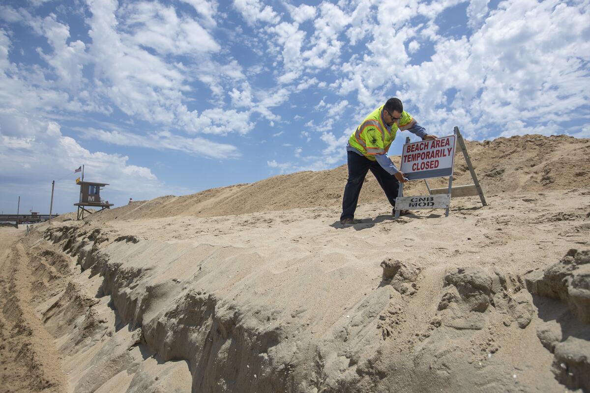 Michael Martinez with the Newport Beach Public Works Department places a sign on a sand berm near Balboa Pier.