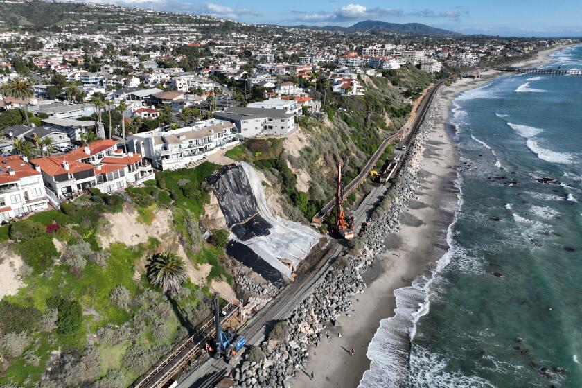 San Clemente, CA - February 27: An aerial view of a landslide near cliff-top homes, protective tarping to prevent further slides from upcoming rain storms and crews building a barrier wall to secure slipping slopes and protect the Metrolink tracks from sliding land in San Clemente Tuesday, Feb. 27, 2024. Multiple landslides have appeared on the ocean front bluffs in the North Beach area. The latest barrier wall will be the third built to secure San Clemente's slipping slopes and protect the tracks from sliding land. Costs are mounting for the continued slope failures. (Allen J. Schaben / Los Angeles Times)