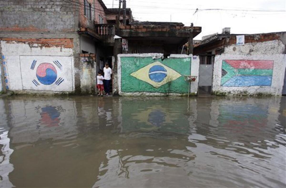Residents stand at the entrance of a house on a flooded street at Vila Itaim neighborhood in Sao Paulo, Brazil, Tuesday, Jan. 11, 2011. Brazilian authorities say heavy rains have triggered mudslides and floods in southeastern Brazil, killing at least 13 people. Sao Paulo state civil defense officials say 11 people died when their houses collapsed because of mudslides and two were killed in flash floods. Painted on walls, from left, a South Korean flag, a Brazilian flag and a South African flag. (AP Photo/Nelson Antoine)