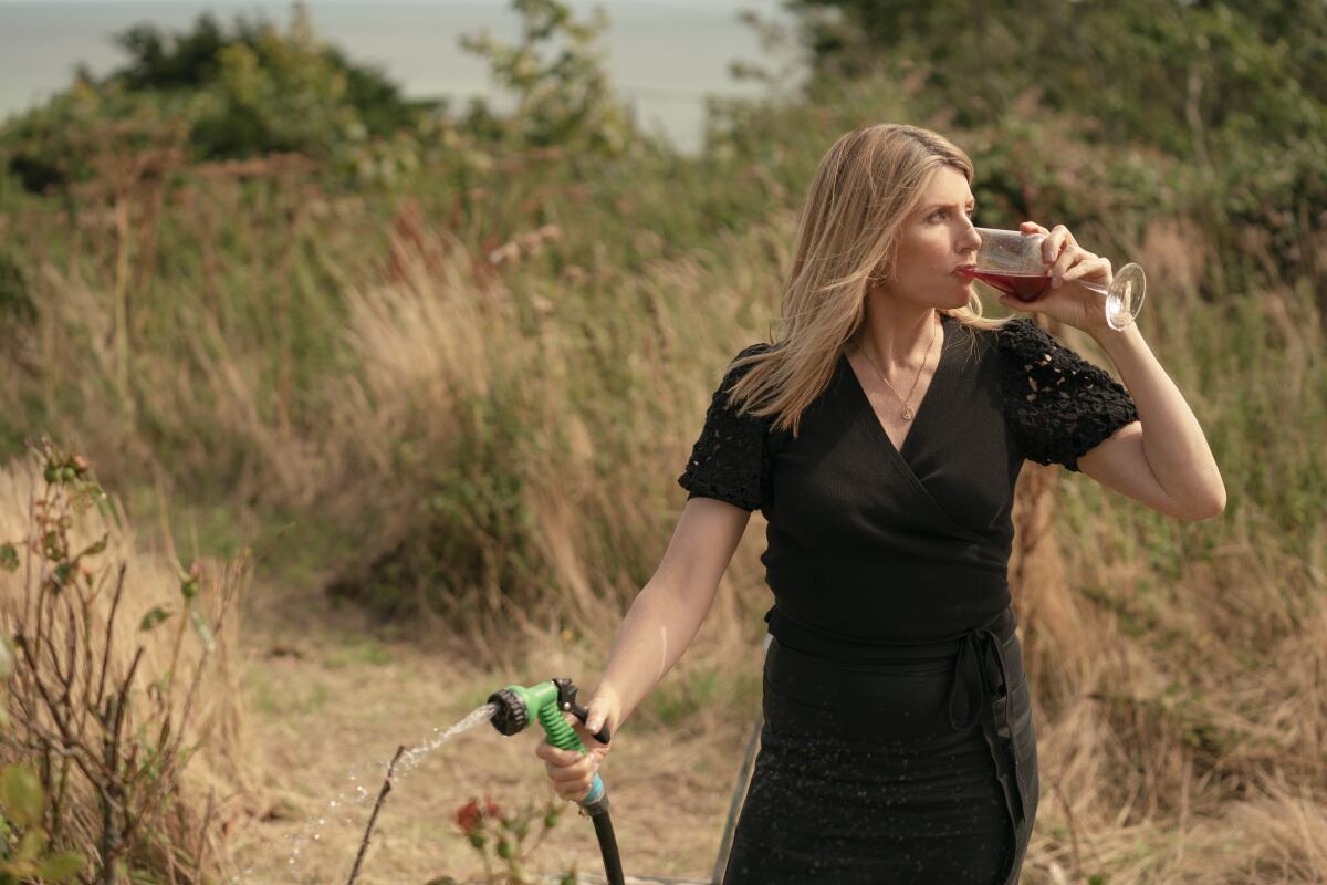 A woman stands outside watering plants while drinking a glass of wine in "Bad Sisters."