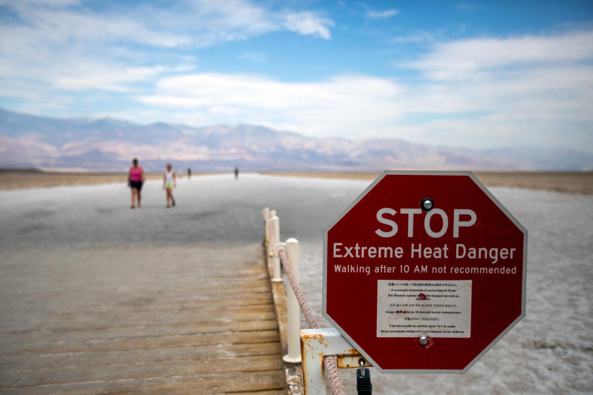 A stop sign warns of extreme heat danger as distant figures walk amid an arid landscape.