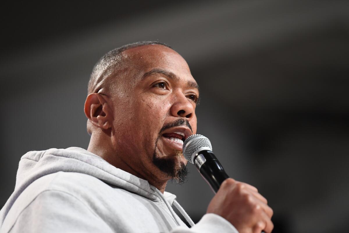 Timbaland holds a microphone to his mouth while clad in a light gray hoodie