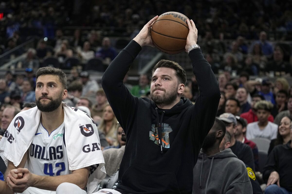 Dallas Mavericks guard Luka Doncic, right, returns the ball to play as he sits on the bench during the first half of an NBA basketball game against the San Antonio Spurs in San Antonio, Wednesday, March 15, 2023. (AP Photo/Eric Gay)