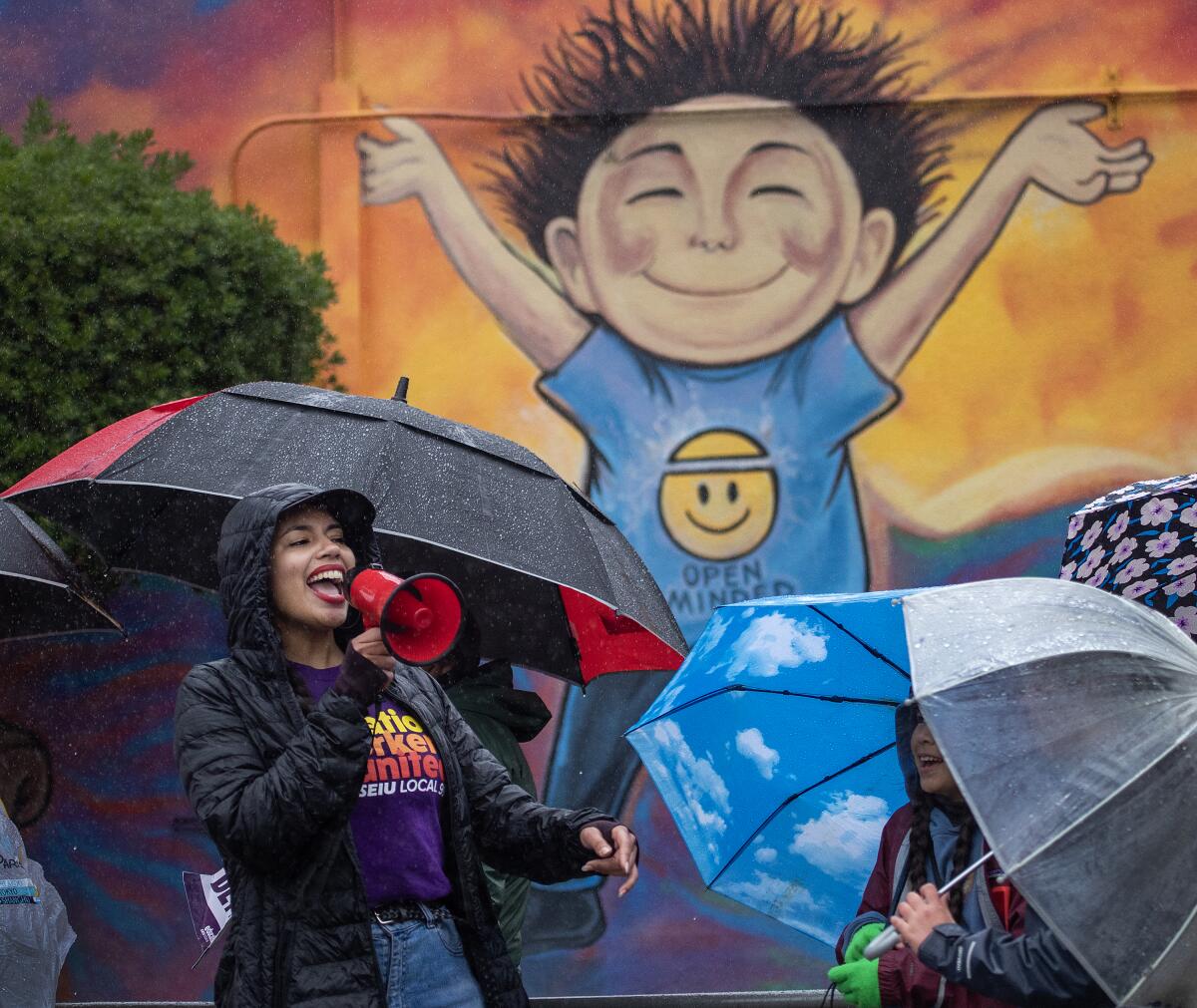 A smiling woman holds a bullhorn in front of a colorful mural of a child. 