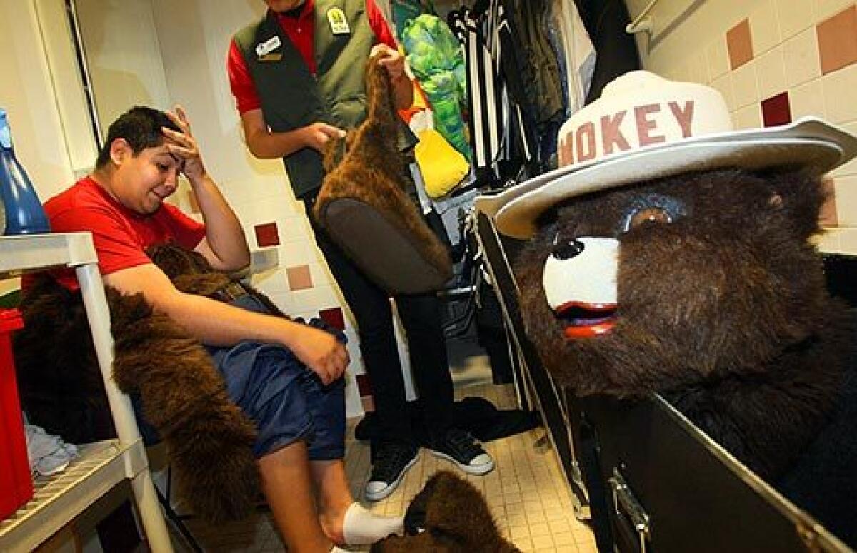 Andrew Garza, 16, a high school senior from Santa Ana, wipes his brow after a session dressed as Smokey Bear at the Discovery Science Center in Santa Ana. Helping Garza pack up the bulky suit is Juan Plascencia, who guides him in crowds because of the costume's limited visibility.