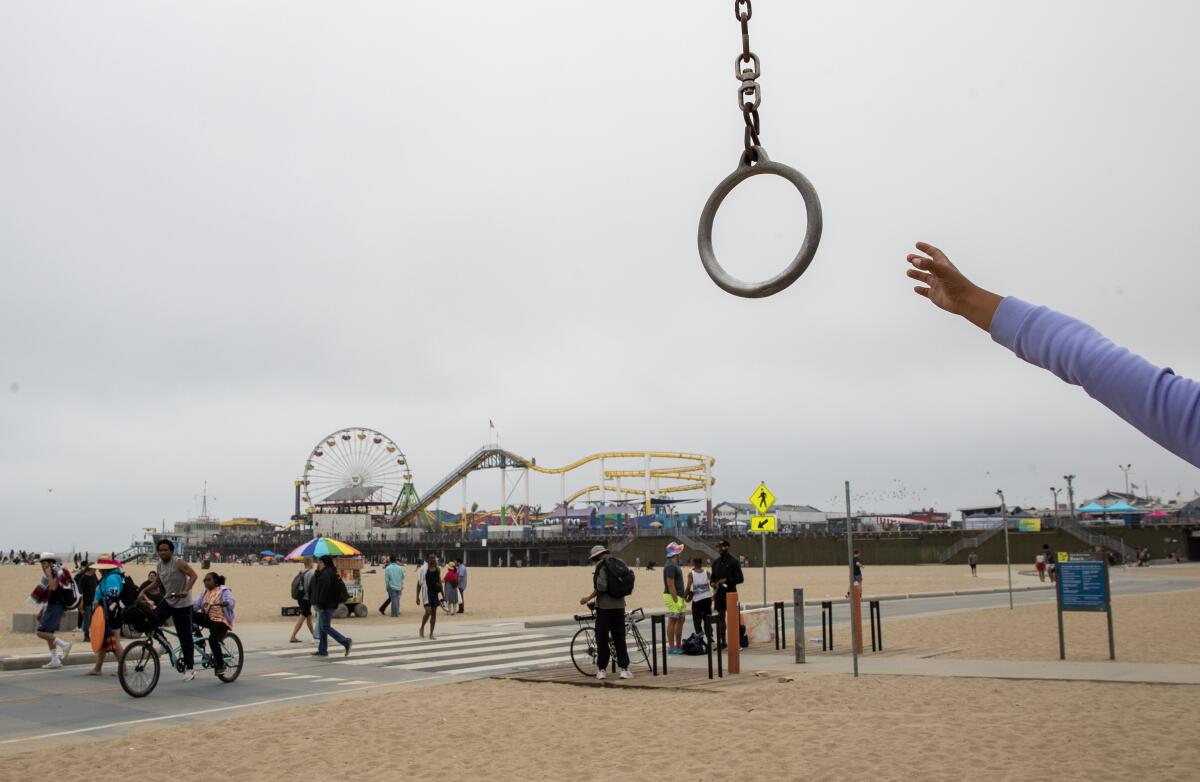 A view of people, some on bicycles, on the beach, with a roller coaster and Ferris wheel in the distance 