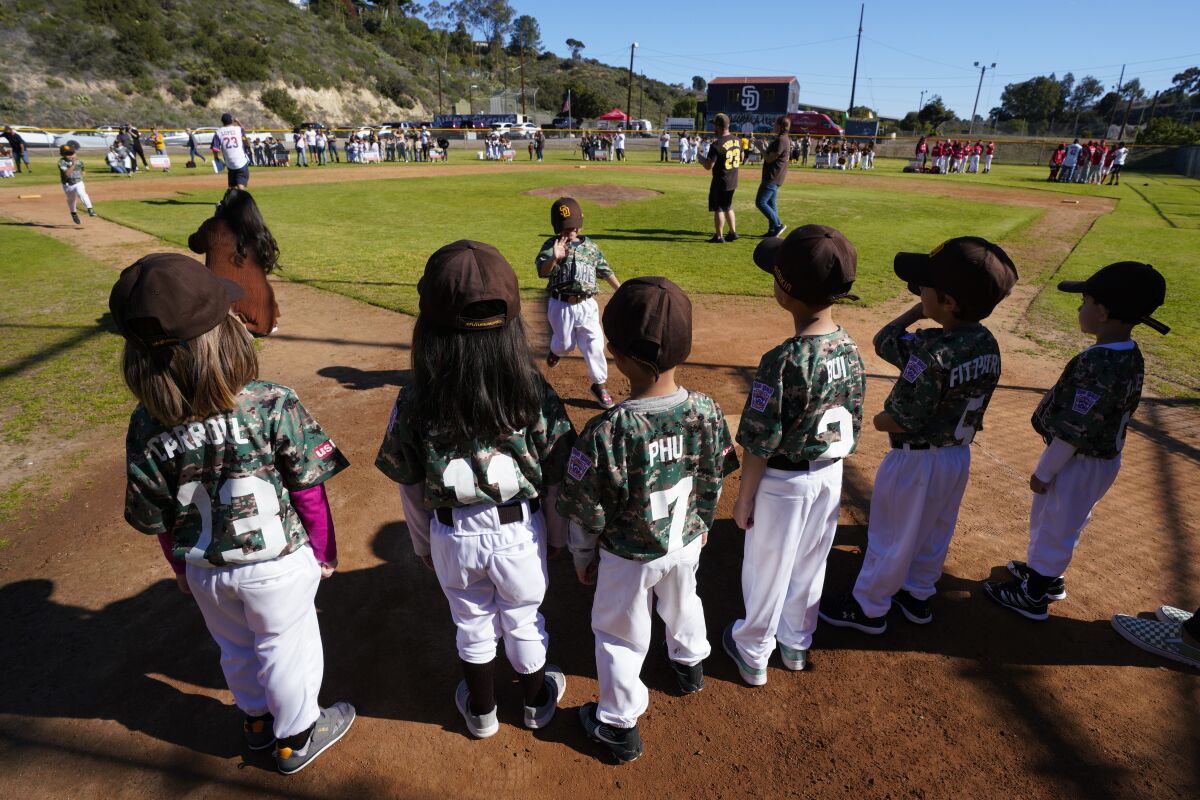 Little League players in camo uniforms line up as teammates run to home base