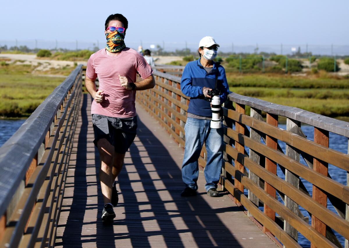 A jogger and a wildlife photographer wear masks at Bolsa Chica Ecological Reserve in Huntington Beach on May 20.