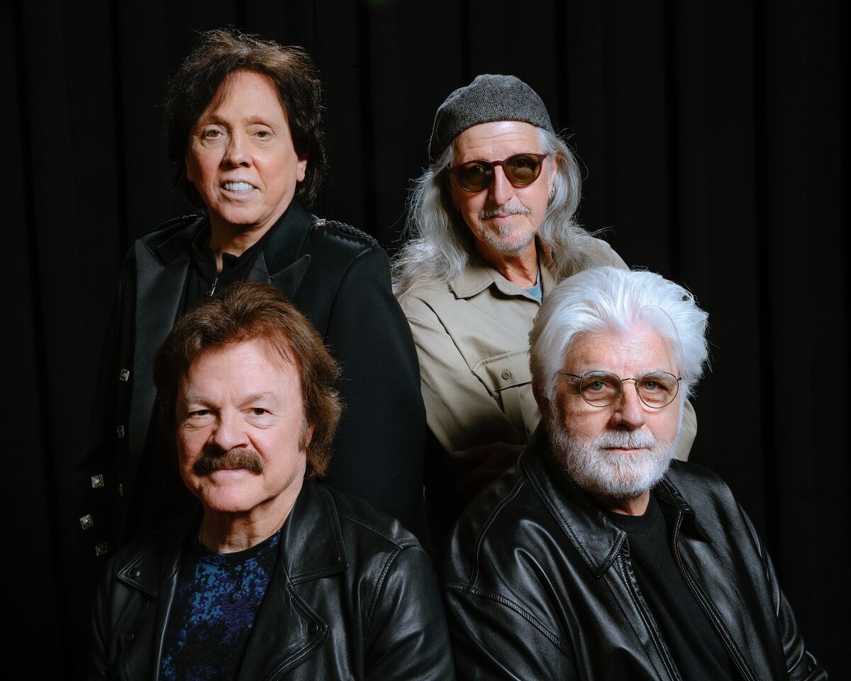Four men in a rock band pose against a black background