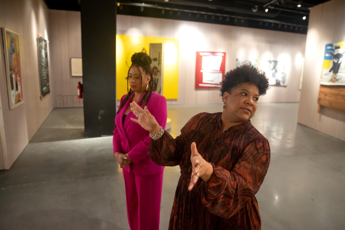 Two women walk among artworks.