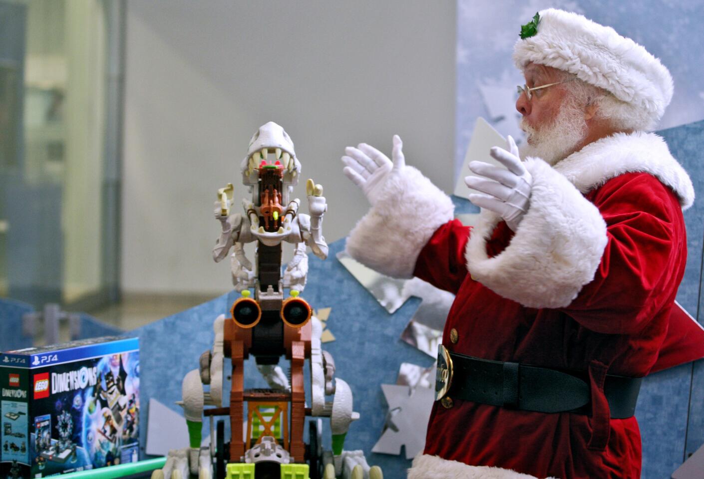 Santa Claus reacts to an electronic dinosaur, available at the Target store, during the annual Glendale Galleria Holiday Retail Gift Panel at the mall in Glendale on Tuesday, November 10, 2015. A wide variety of other sample gifts were shown by different mall retailers as well.