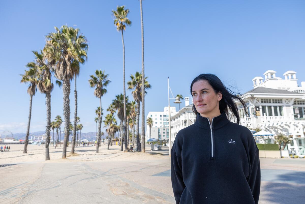 A woman in a black sweat top stands on a breezy beach near an upscale white hotel.