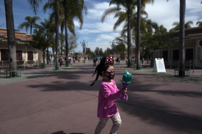 ANAHEIM, CA - MARCH 17: Wearing a face mask, Bliss Cordova, age 2 1/2, of Chino, runs around Downtown Disney chasing bubbles on Wednesday, March 17, 2021 in Anaheim, CA. More than a year after closing due to the pandemic, the theme parks at the Disneyland Resort in Anaheim are scheduled to open April 30 with limited capacity and restrictions on some attractions. (Francine Orr / Los Angeles Times)