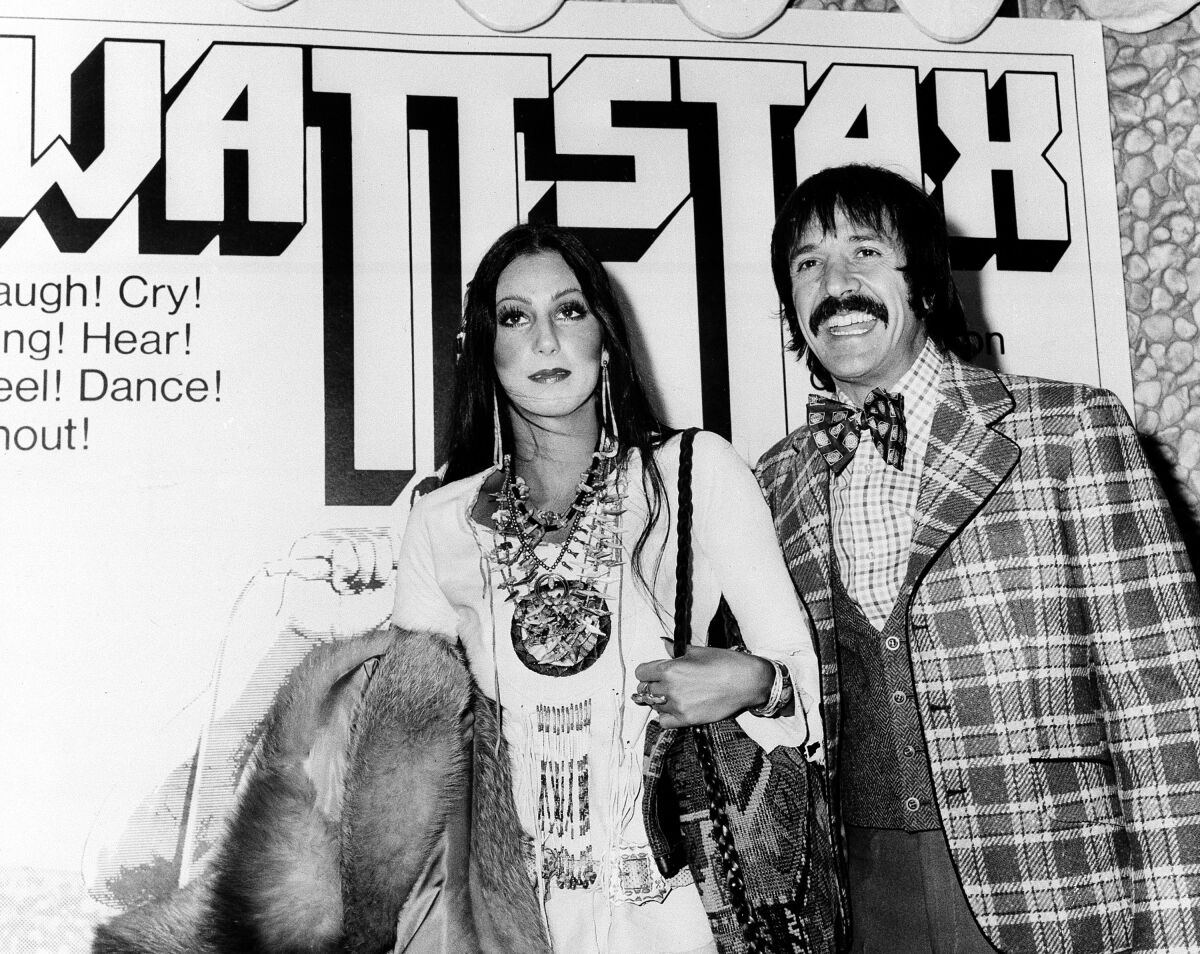 Cher and Sonny Bono are shown in front of a poster of the documentary-movie Wattstax