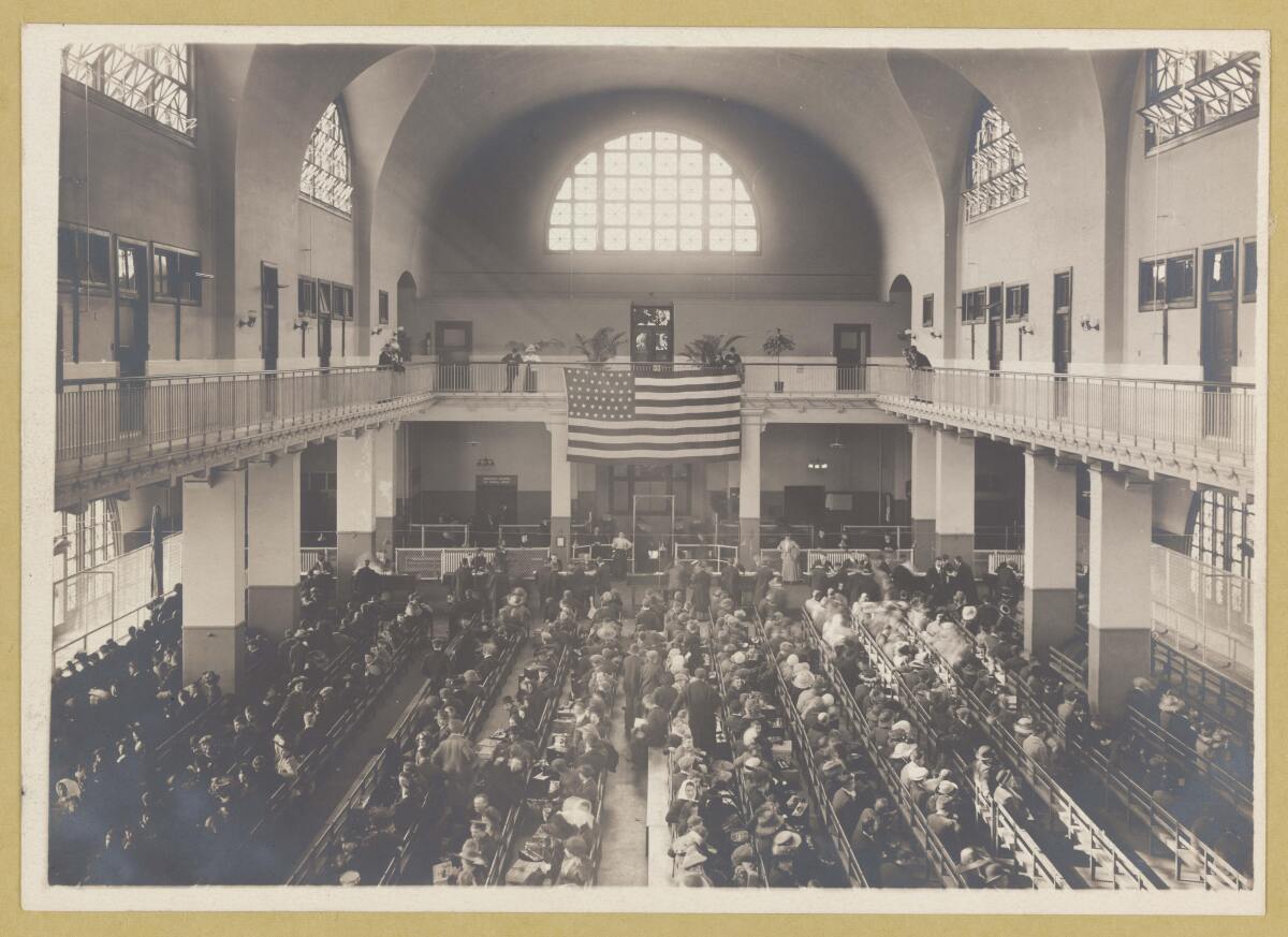 A black-and-white photo of rows of people seated in a building with high ceilings.