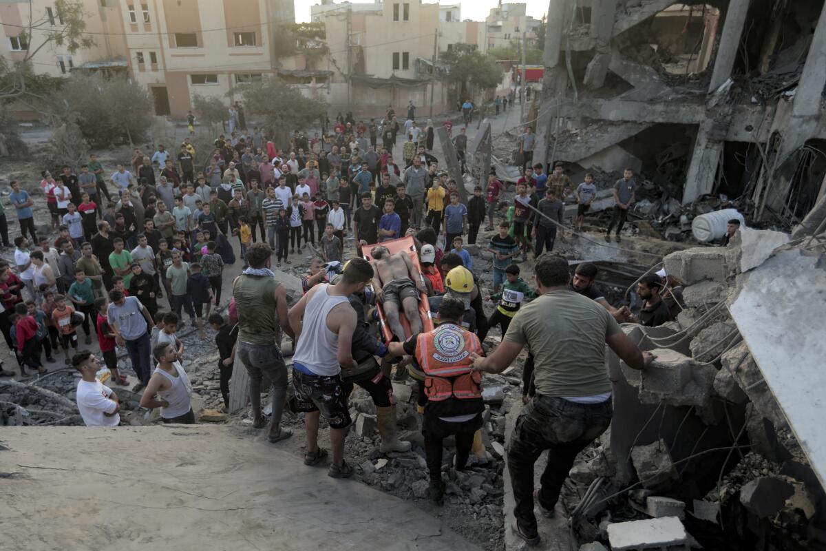 People move a wounded man with a crowd watching, surrounded by rubble