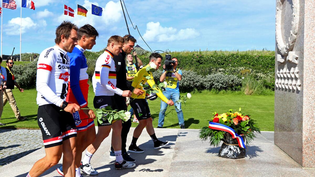 Tour de France leader Mark Cavendish (yellow jersey) and his cycling teammates place flowers at the Utah Beach Peace Monument in Normandy.