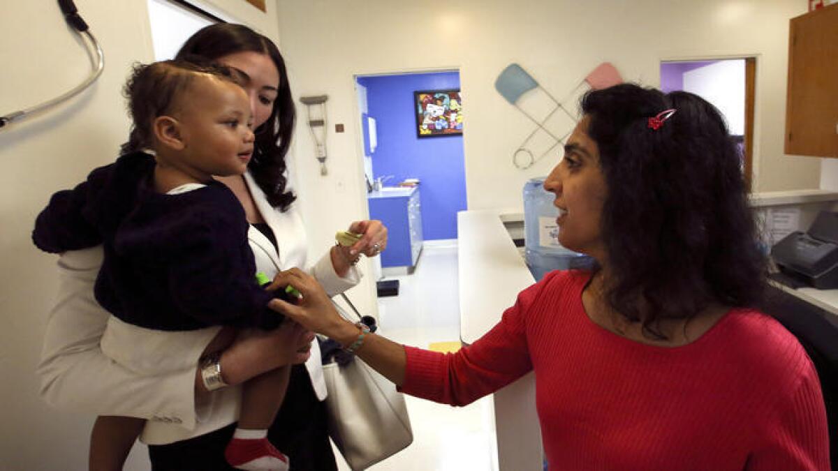 Monica Asnani, a la derecha, le dice adios a Kristian Richard, de1 año, mientras es sostenido por su mamá, Natasha, despues de que el niño recibio la vacuna del sarampion, paperas y rubeola en Medical Arts Pediatric Med Group en Wilshire Boulevard en Los Angeles.