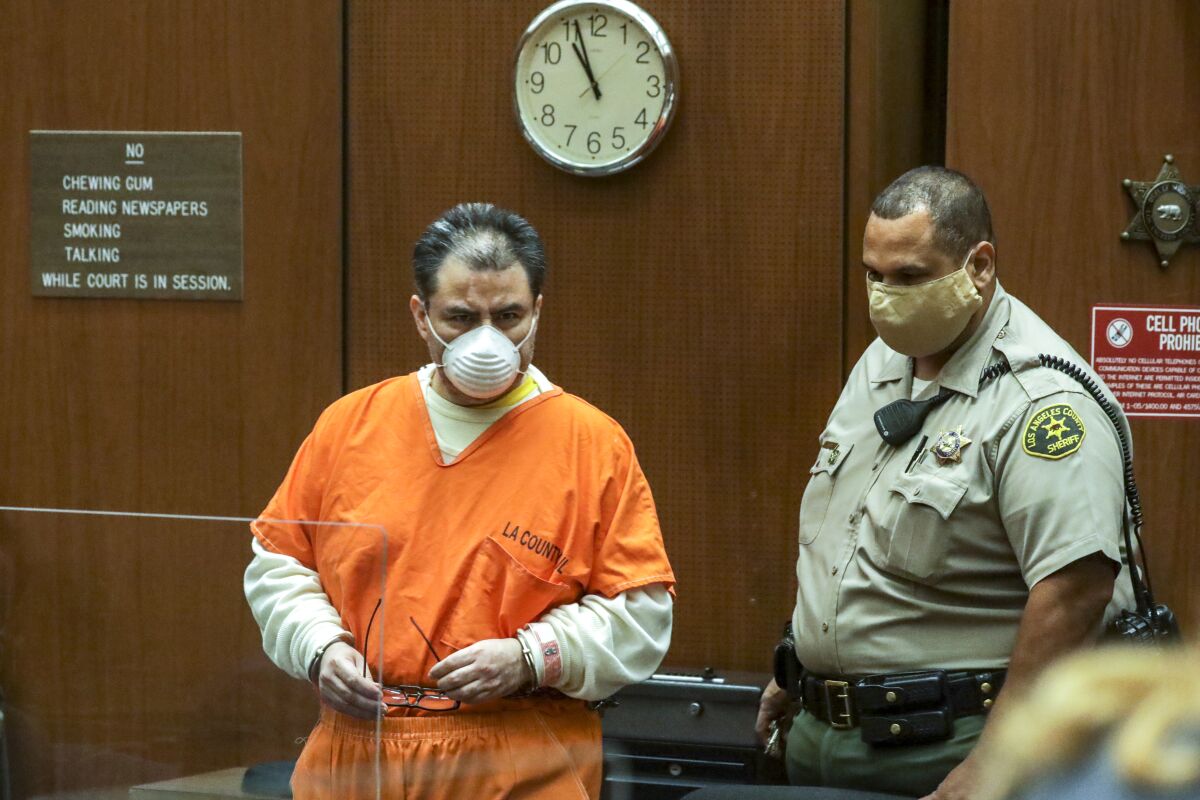A man in court wears an orange jumpsuit and a mask.