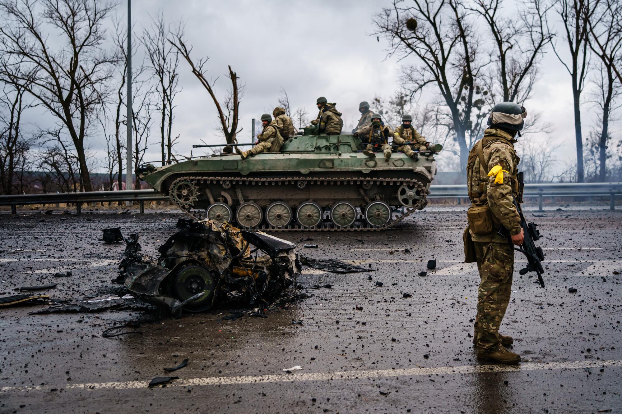 Uniformed troops ride a military vehicle on a debris-littered road