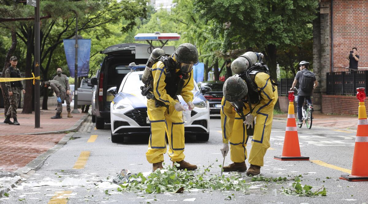 Soldiers wearing protective gear inspect debris on a street 