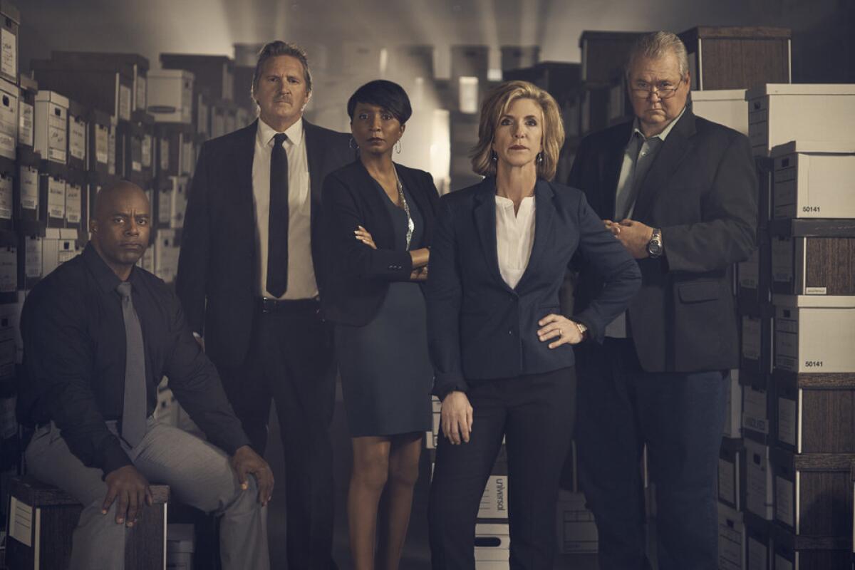 Five men and women wearing business clothing pose in an office filled with file boxes