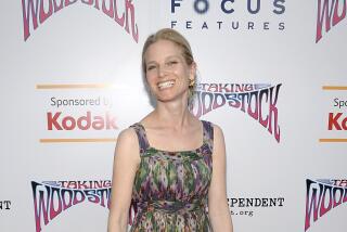 Bridget Fonda in a green and purple patterned dress posing on a red carpet