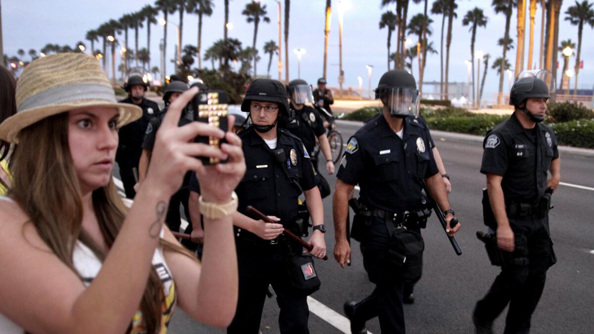 A woman takes photos as a large police force gets into position to fend off rioters along Pacific Coast Highway in downtown Huntington Beach following the US Open of Surfing contest finals on July 28, 2013.