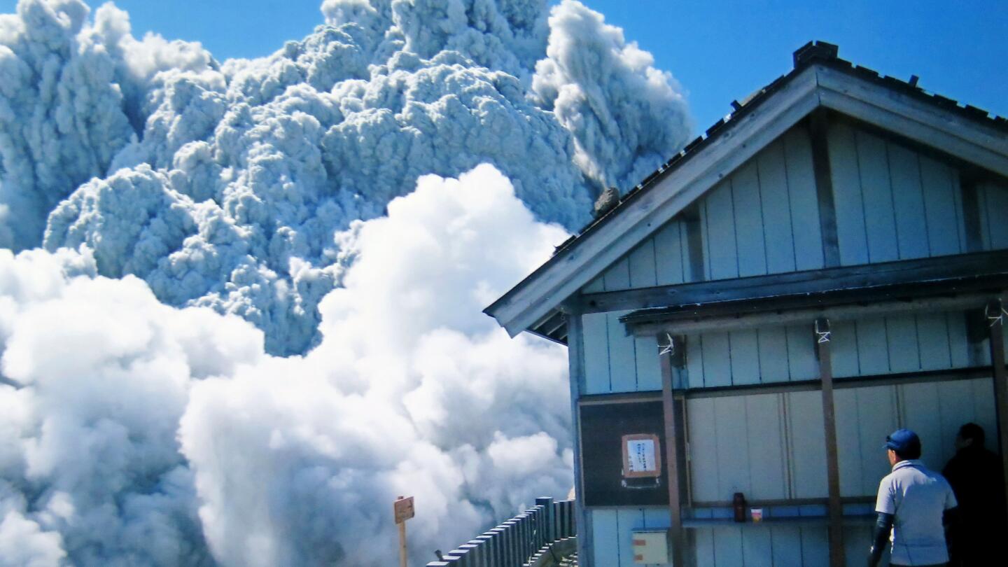 In this photo taken Sept. 27, 2014 by 59-year-old hiker Izumi Noguchi one of at least 47 who fell victim to the eruption of Mount Ontake, a hiker watches dense plumes of gases and ash gushing out from the summit crater as the volcanic mountain starts to erupt.
