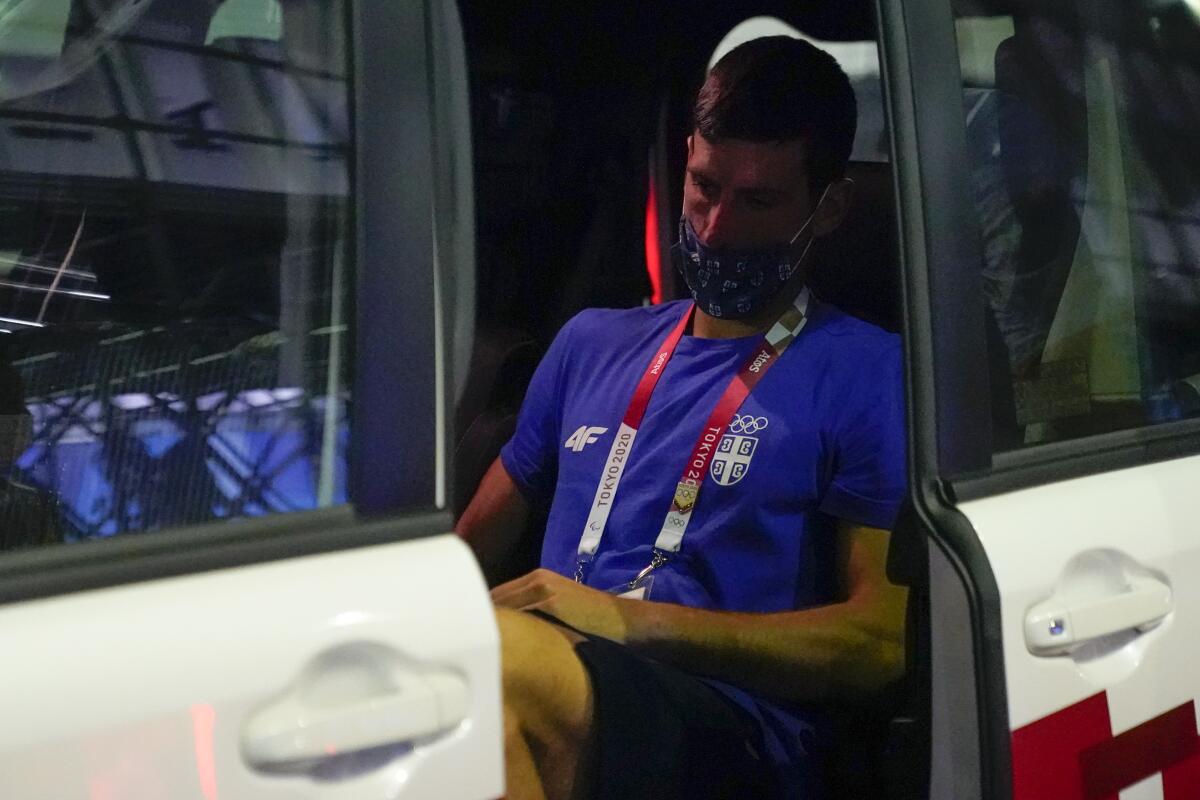 Novak Djokovic sits in a vehicle with his head down.