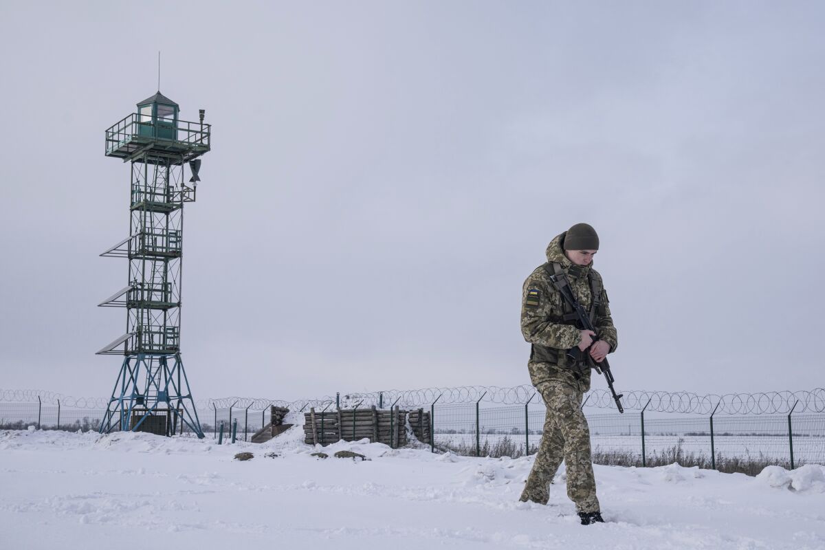 A Ukrainian soldier walks in the snow near a barbed-wire-topped fence