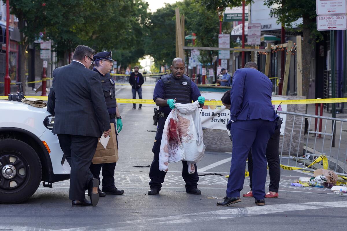 Investigators stand on a street. One holds a bloody white jacket.