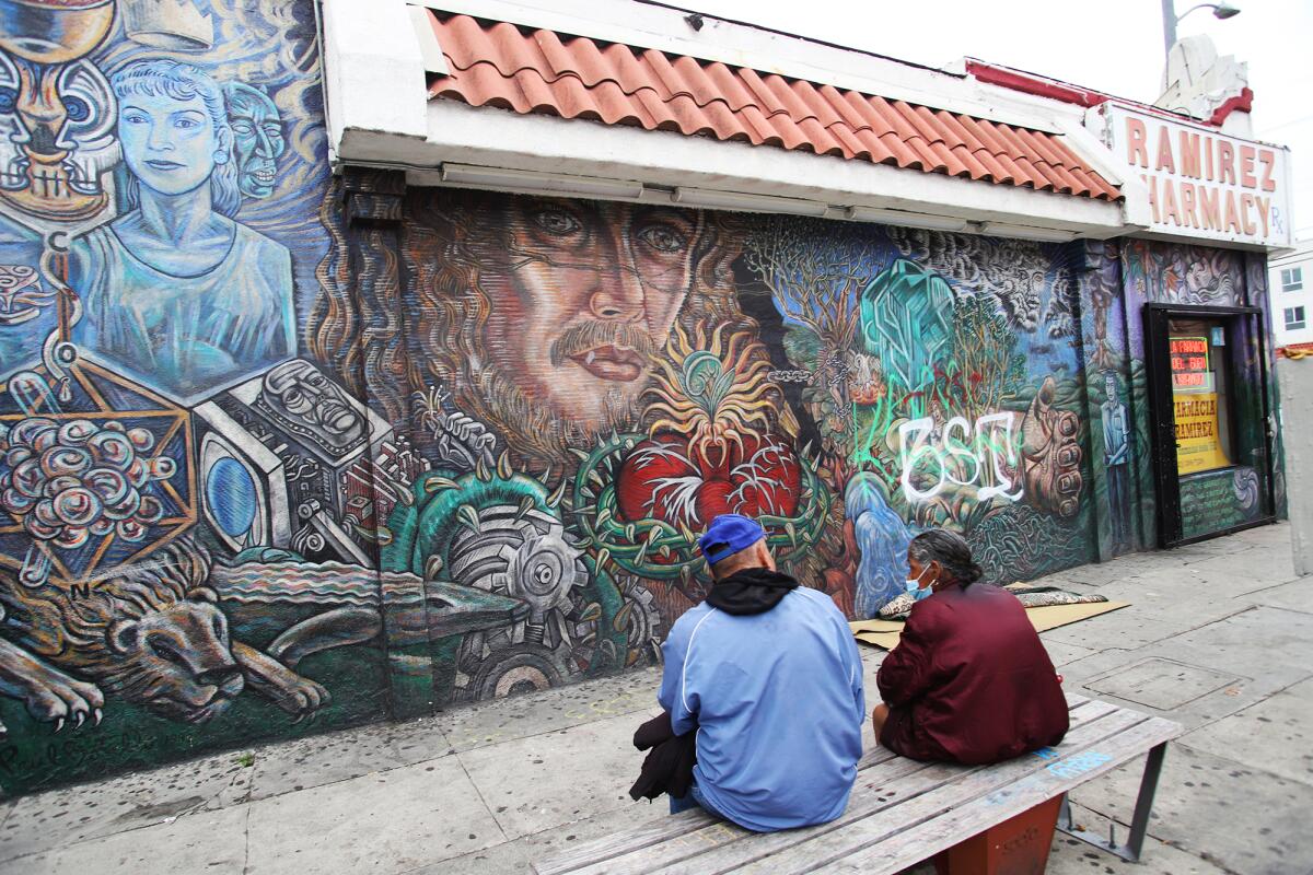 Two people sit on a bench looking at a mural on the side of a pharmacy.