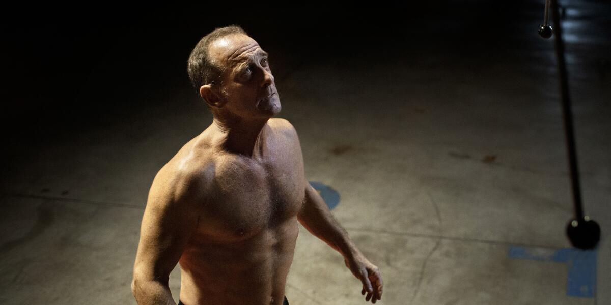 A bare-chested man looking upward in the movie "Titane."