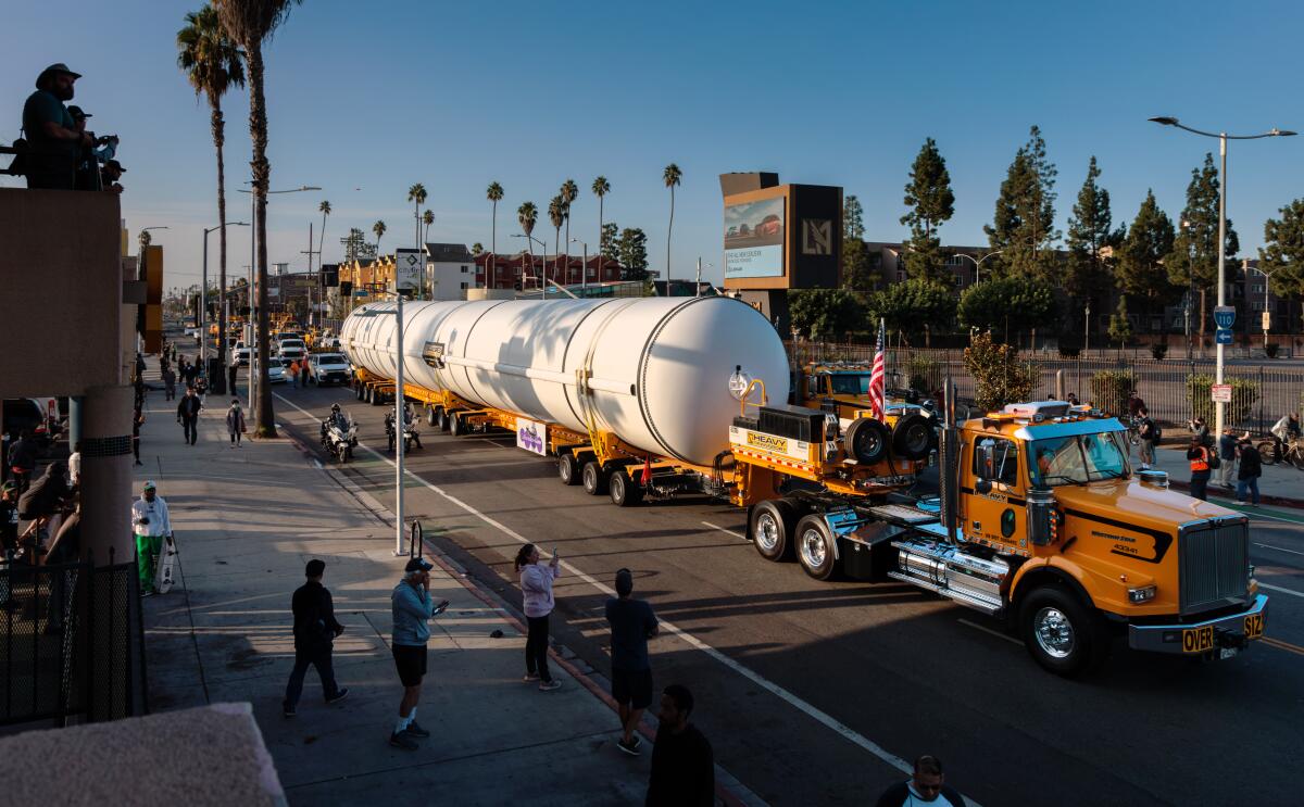 A truck carries a long white metal cylinder.