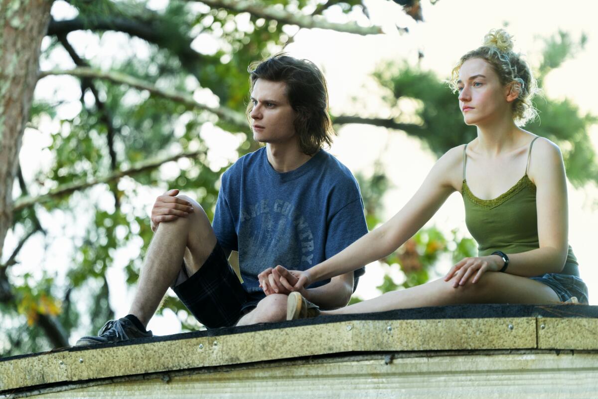 A young man and woman hold hands as they chat sitting atop a trailer home in a scene from "Ozark."