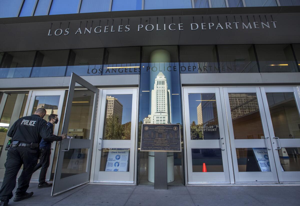 Two officers walk into LAPD headquarters with City Hall reflected in the doors.