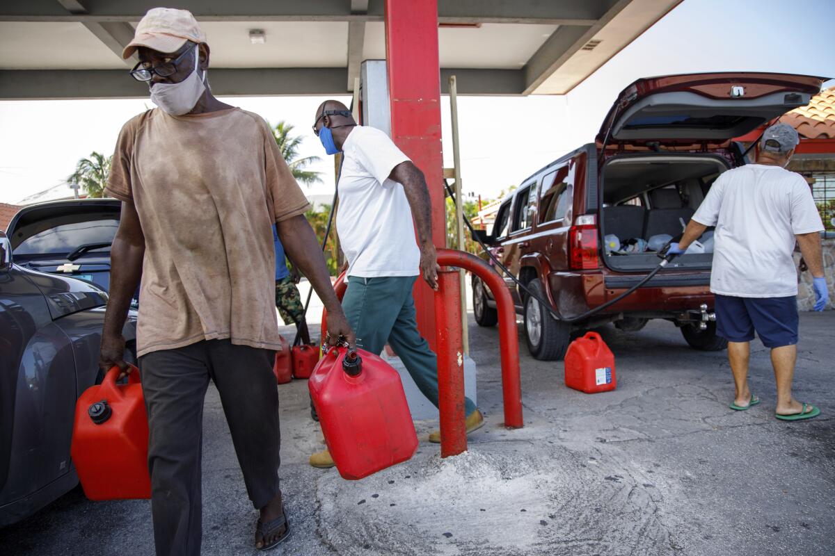 A resident walks with containers filled with gasoline at Cooper's gas station before the arrival of Hurricane Isaias.