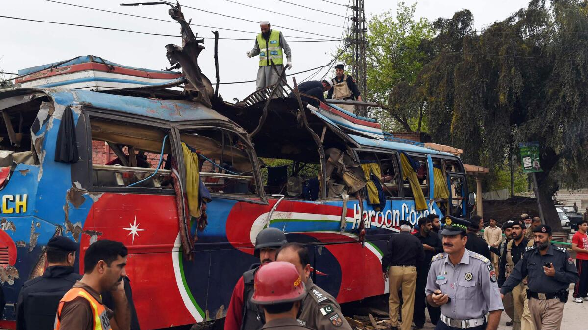 Pakistani volunteers and security forces inspect a destroyed bus after a bomb blast in Peshawar on March 16, 2016.