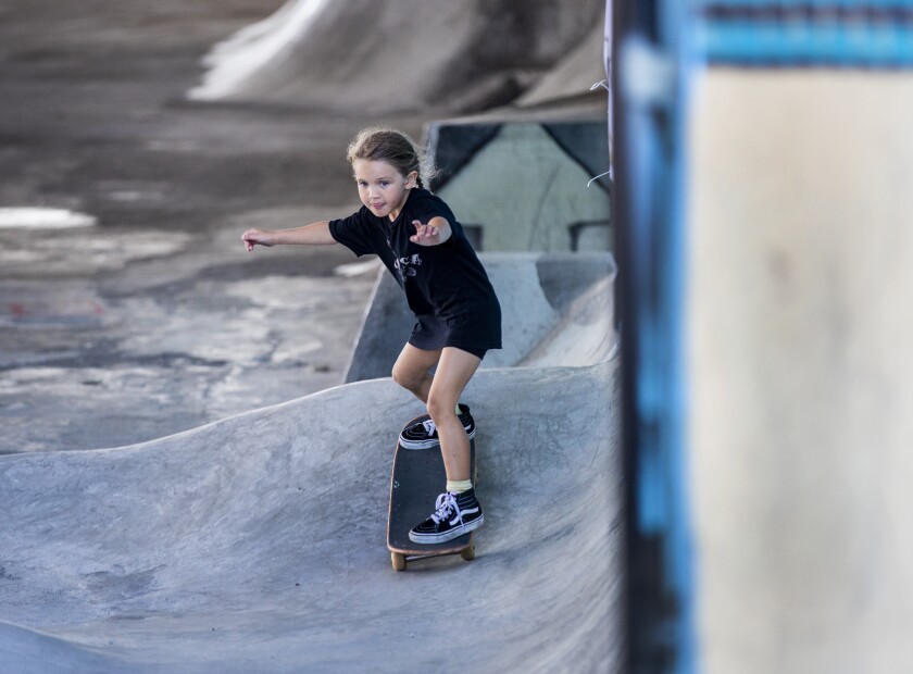 A young girl rides a skateboard at a park.