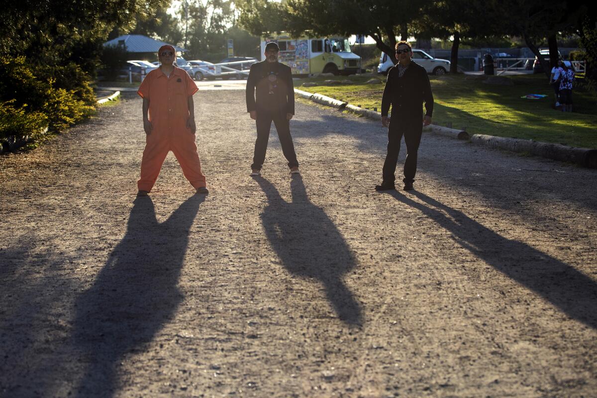 The three members of the Culture Clash stand on a pathway in Elysian Park, their forms casting long shadows.