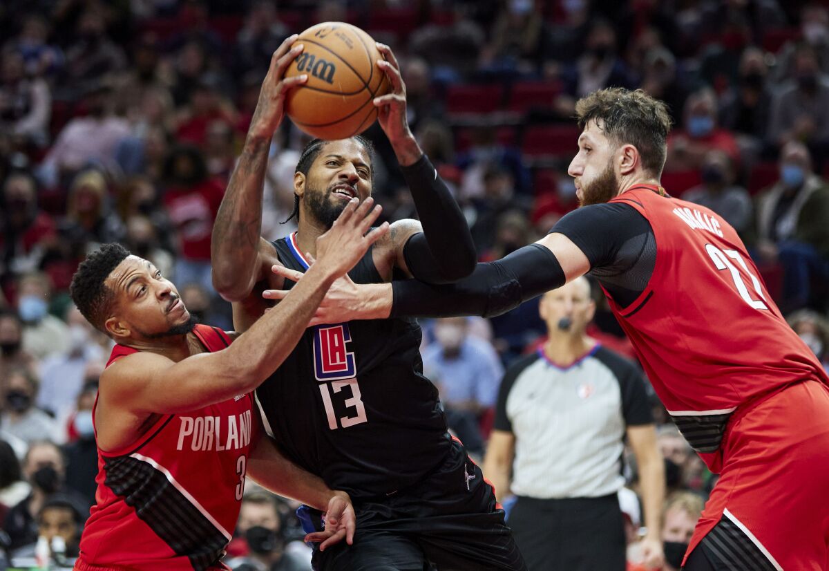 Clippers guard Paul George drives to the basket between Portland Trail Blazers guard CJ McCollum and center Jusuf Nurkic.