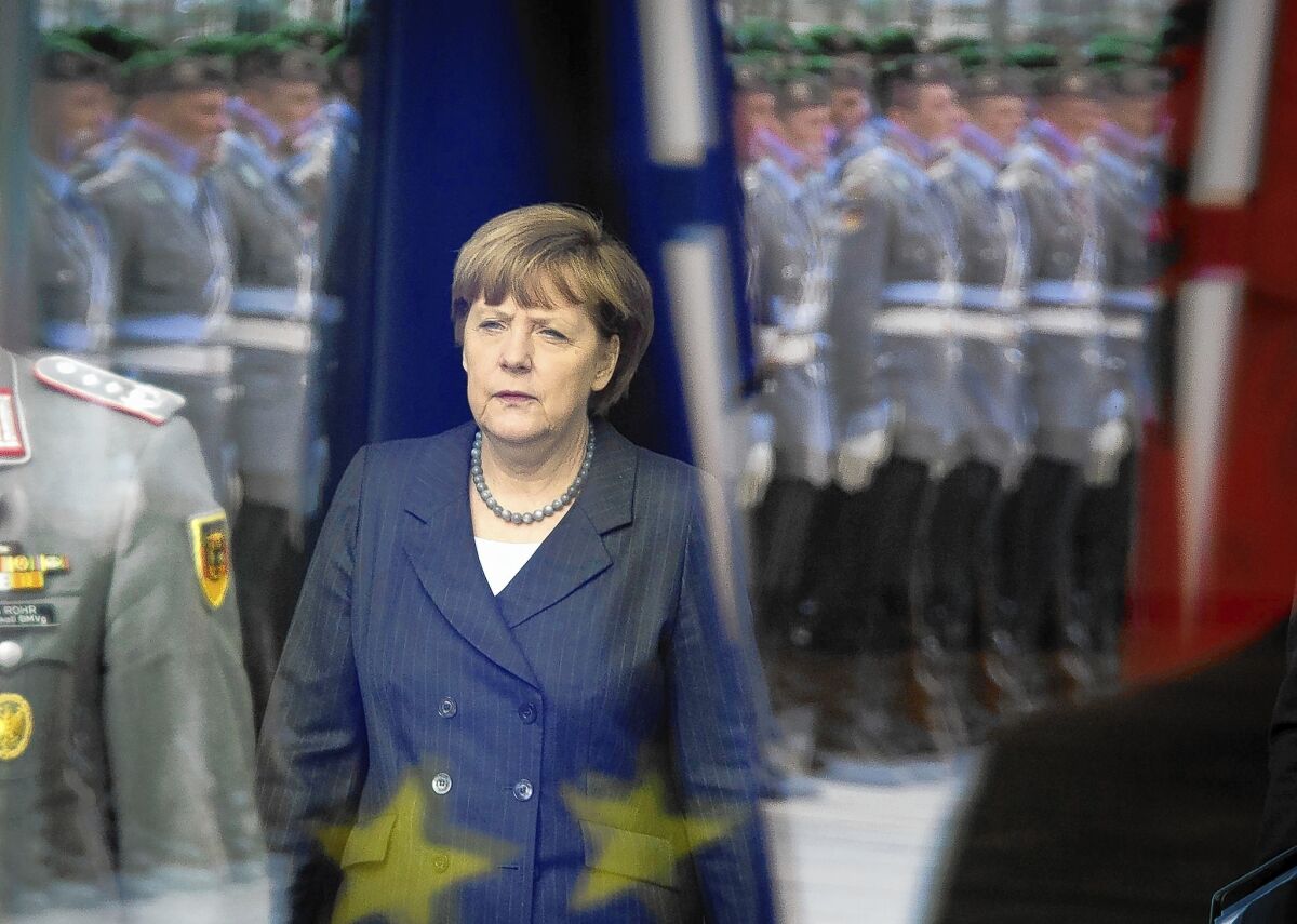 German Chancellor Angela Merkel is seen through a window reflecting an honor guard as she awaits an arrival at the chancellery in Berlin.