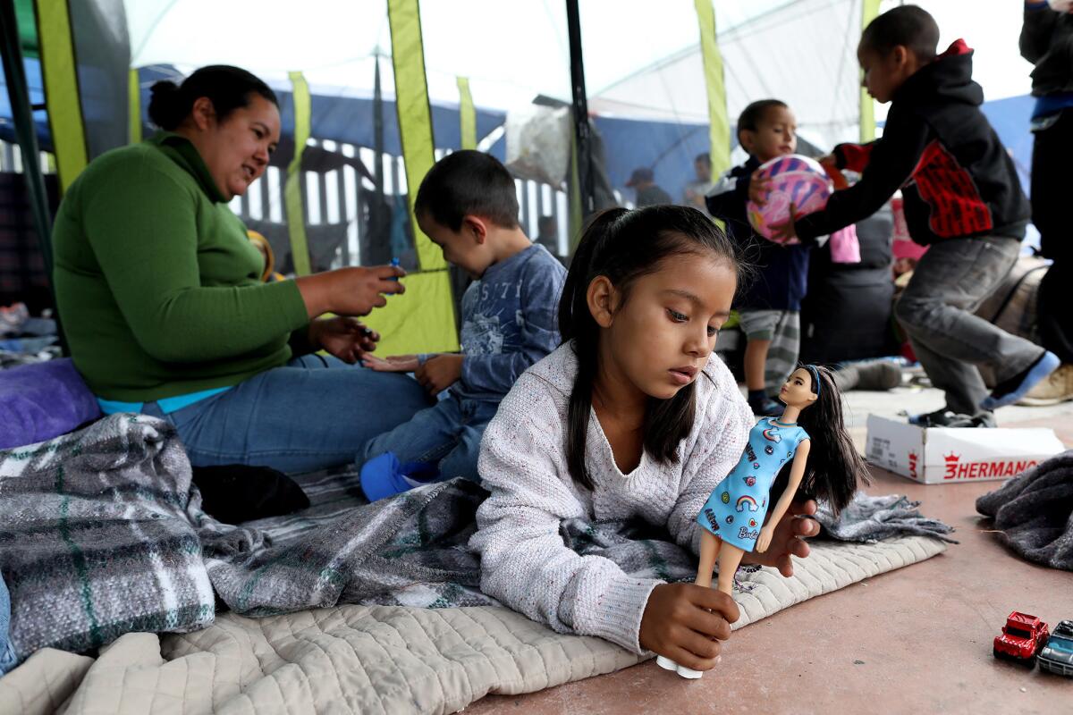 Suany Rodriguez, 6, plays with a doll as her mother and brother sit behind her at a camp in Tijuana. Her mother, Irma Rivera, fled Honduras with the kids after the father was killed and she received a death threat.