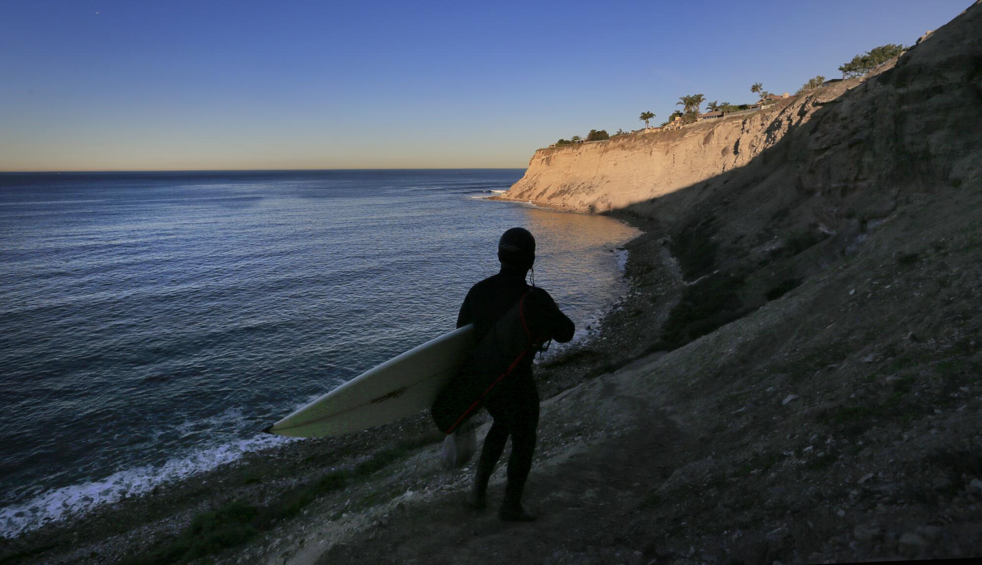 A man walks along the ocean shoreline holding a surfboard.